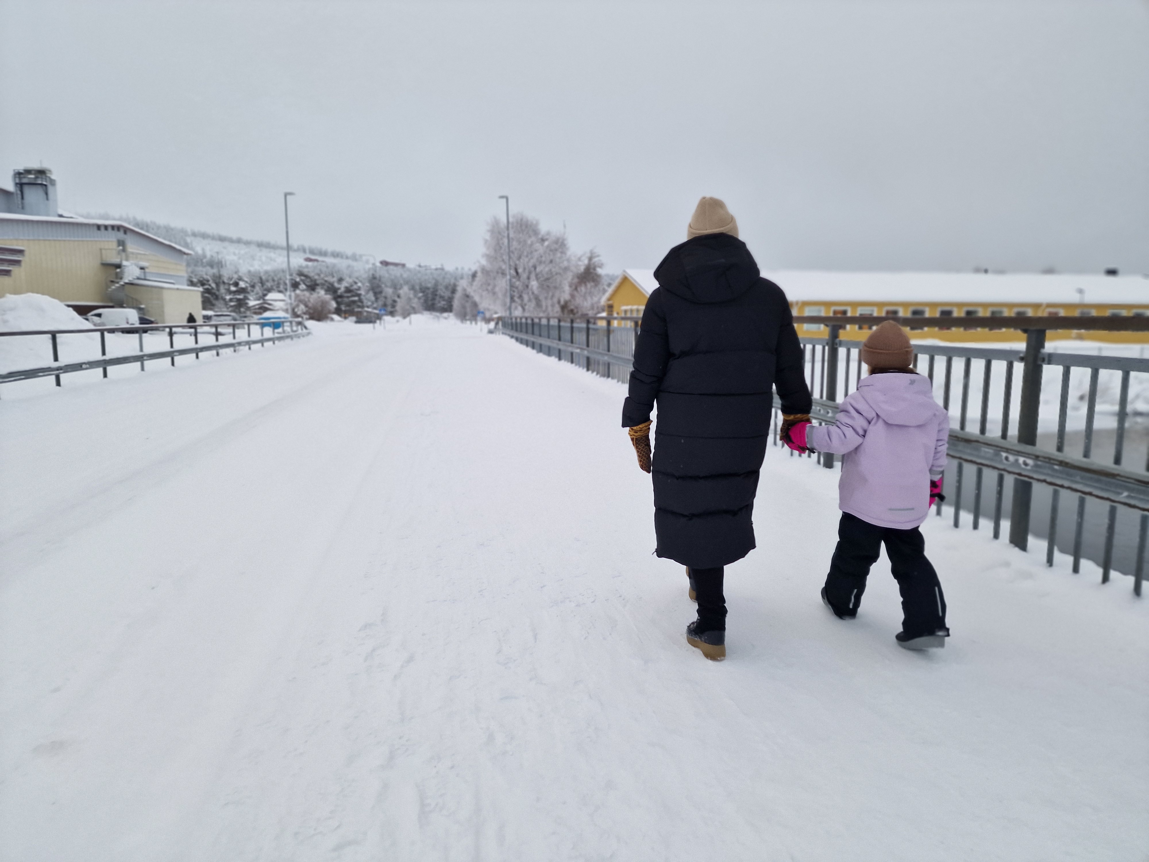 Mor och barn som går hand i hand över en snöklädd bro, på väg mot Öbergaskolan.